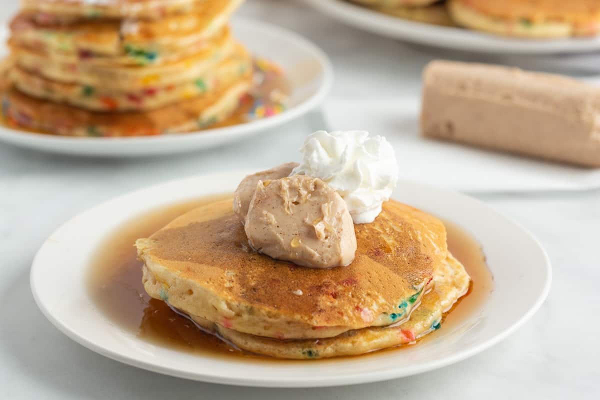 Vista próxima de manteiga de maple e canela e chantilly em uma pilha curta de panquecas.