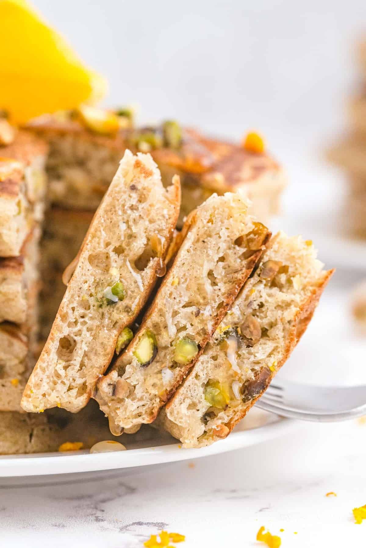 Close up de pedaços de panquecas mostrando pistaches, a pingar mel.