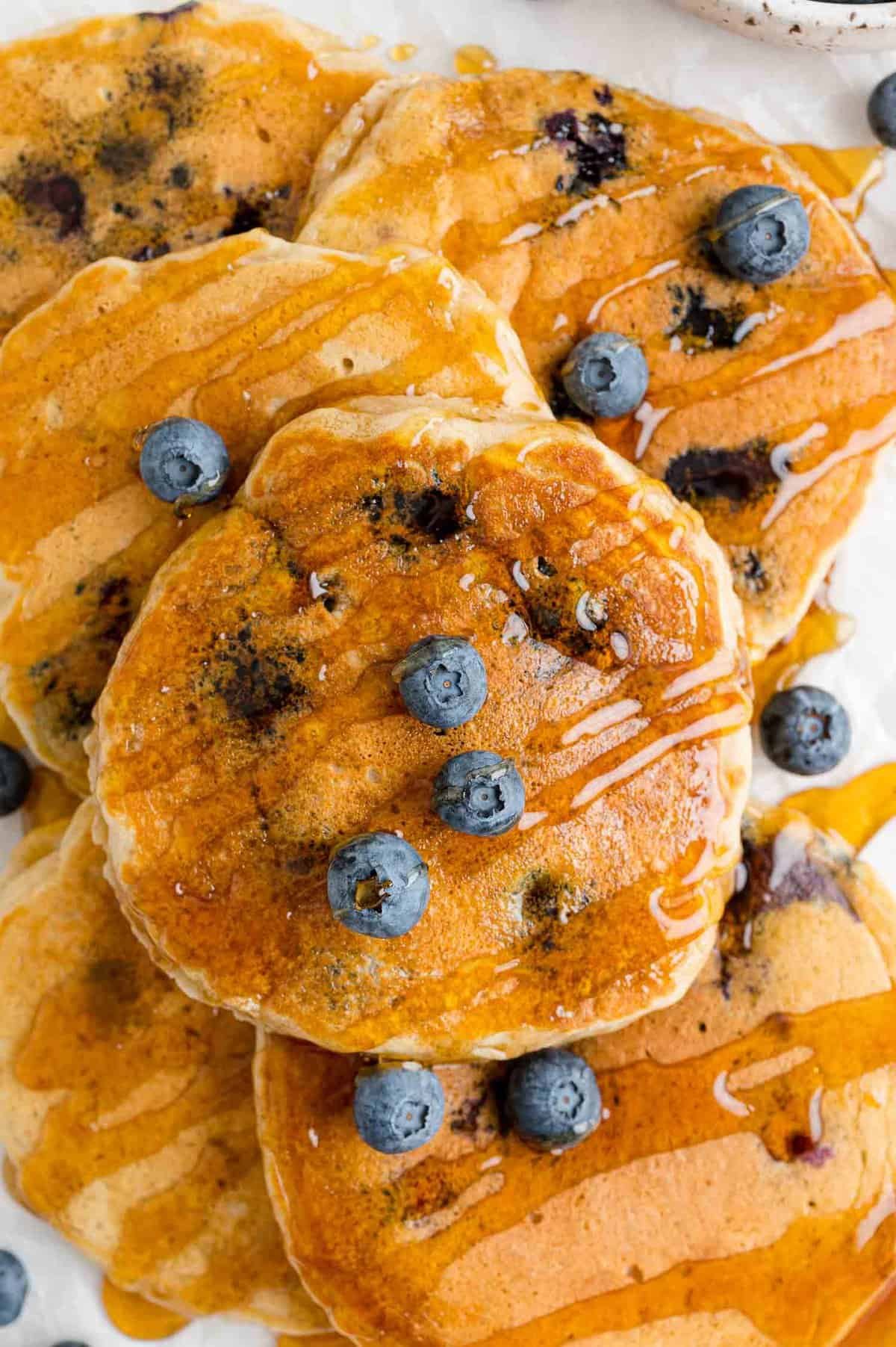 Pilha de panquecas de mirtilo com soro de leite coalhado cobertas com xarope e mirtilos.