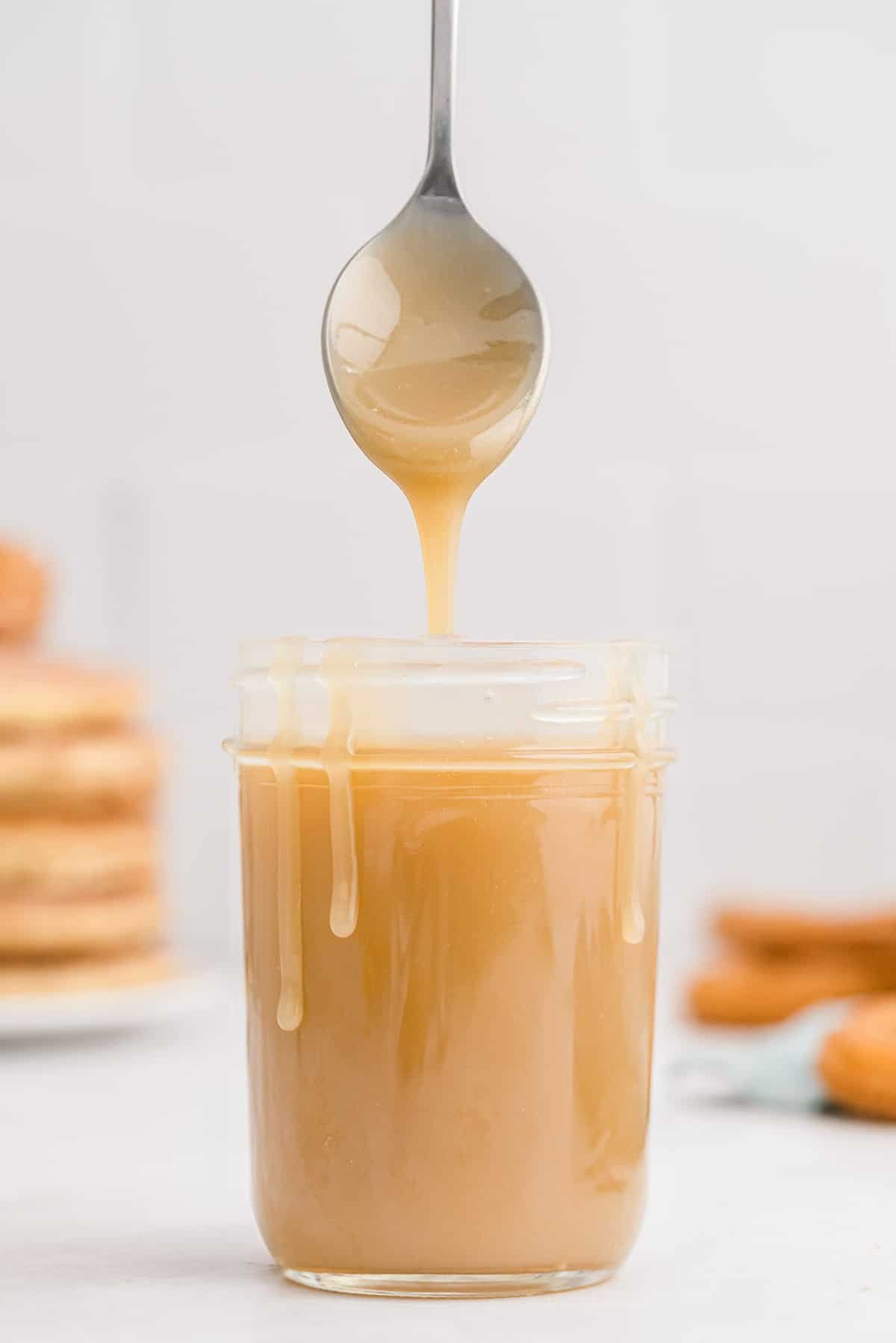 Caramelo em um pote, escorrendo pelos lados do pote, uma colher pairando sobre.