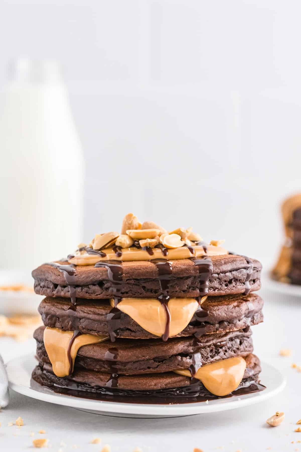 Pilha de panquecas escorrendo com xarope de chocolate e manteiga de amendoim derretida.