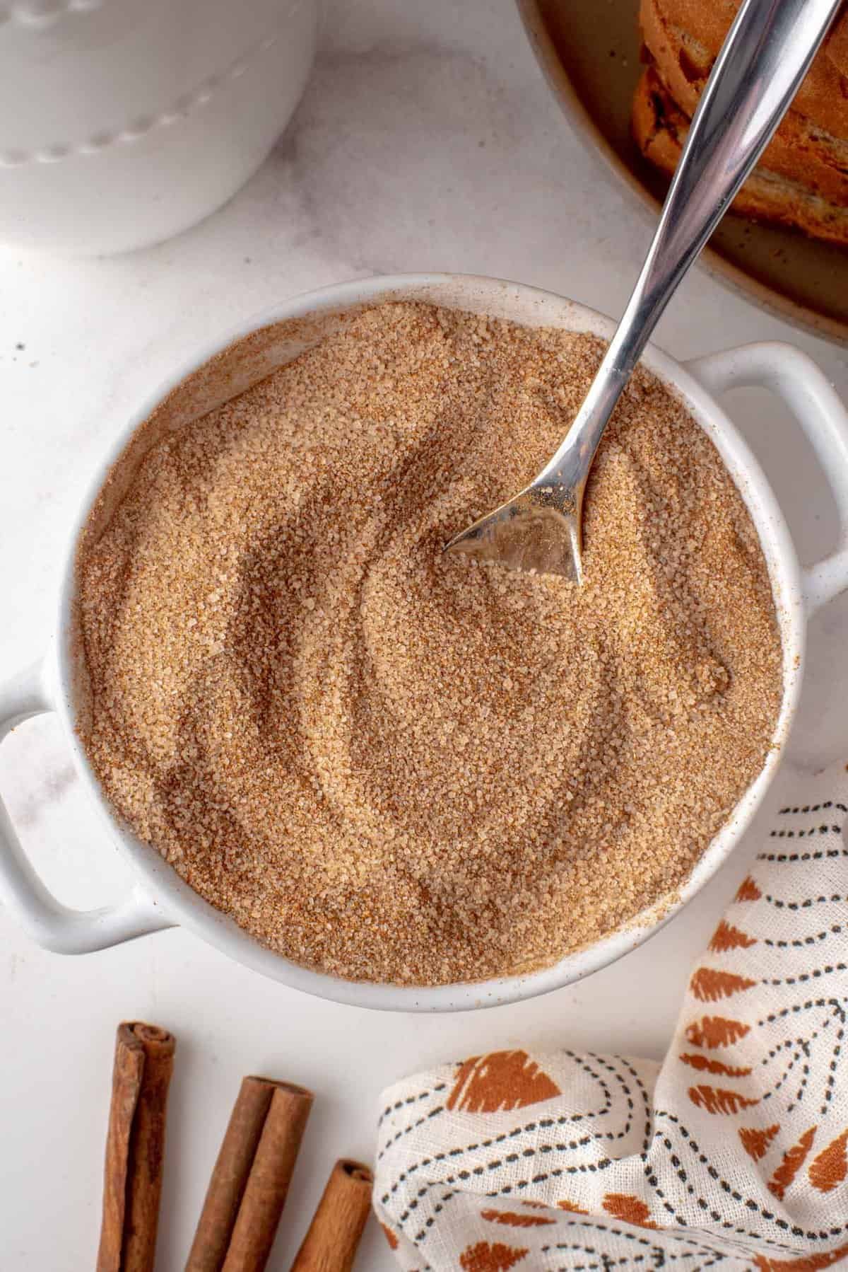 Açúcar e canela em uma pequena tigela branca com colher de prata.