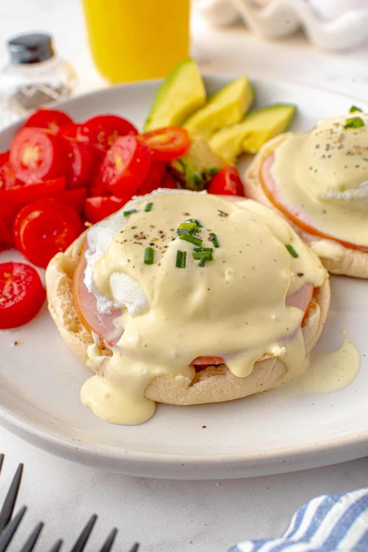 Ovos Benedict em um prato branco com tomate e abacate.