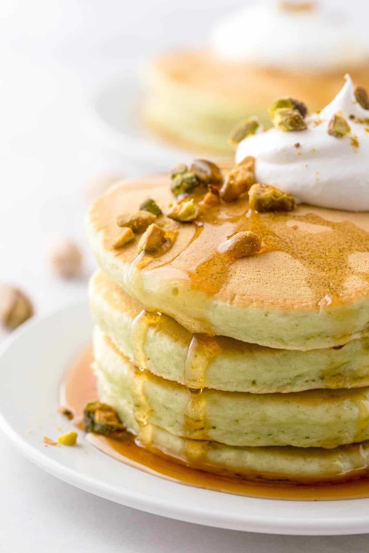 Pequena pilha de panquecas verdes claras, escorrendo com calda e cobertas com pistachios.