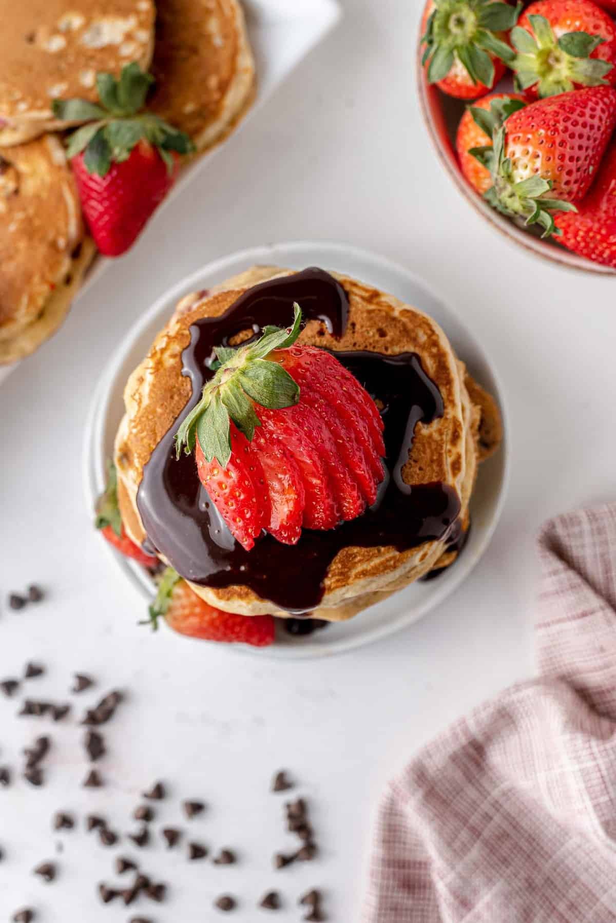 Visão aérea de uma pilha de panquecas com xarope de chocolate e morangos.