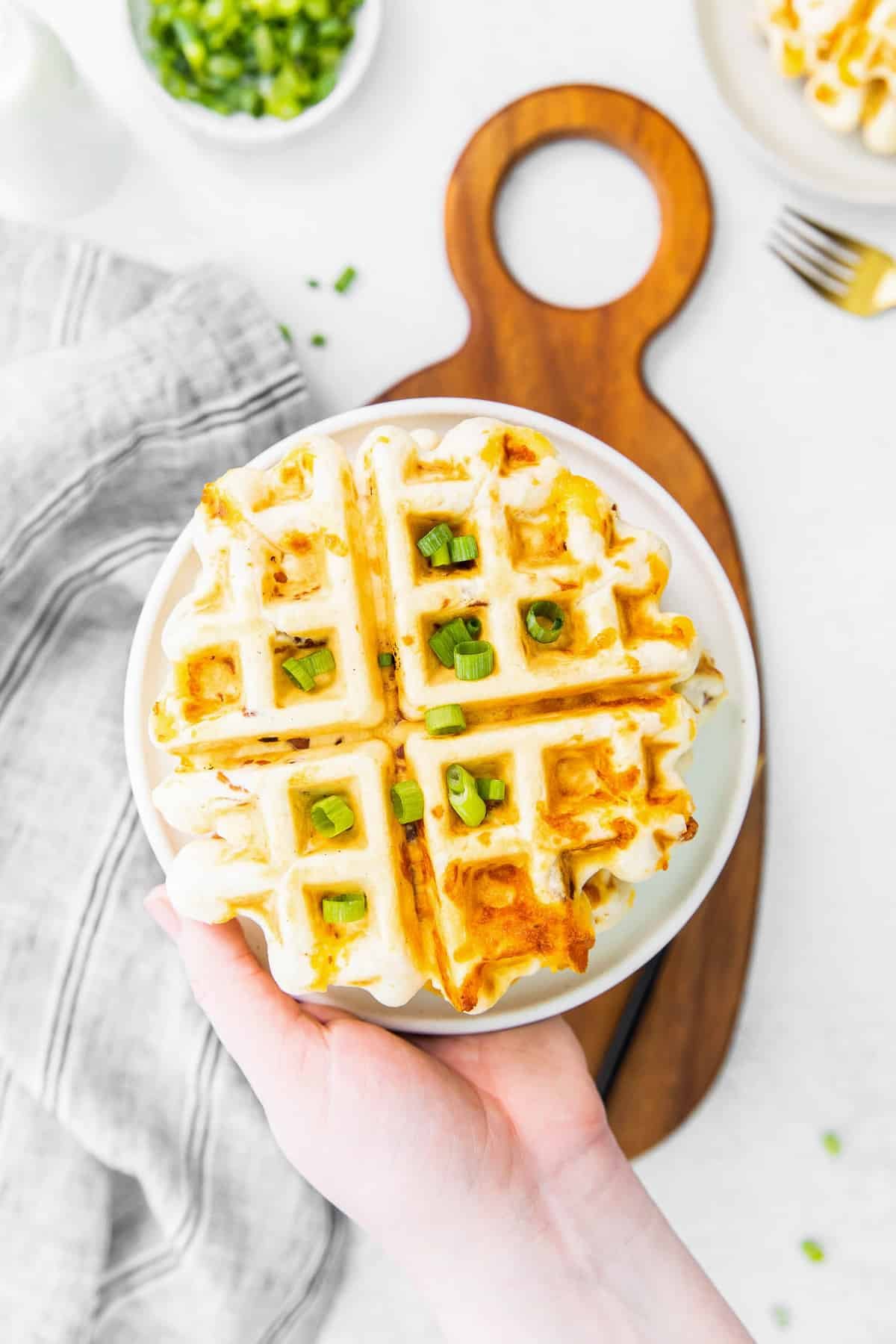 Waffle coberto com queijo cheddar e cebolinha verde, em um prato.