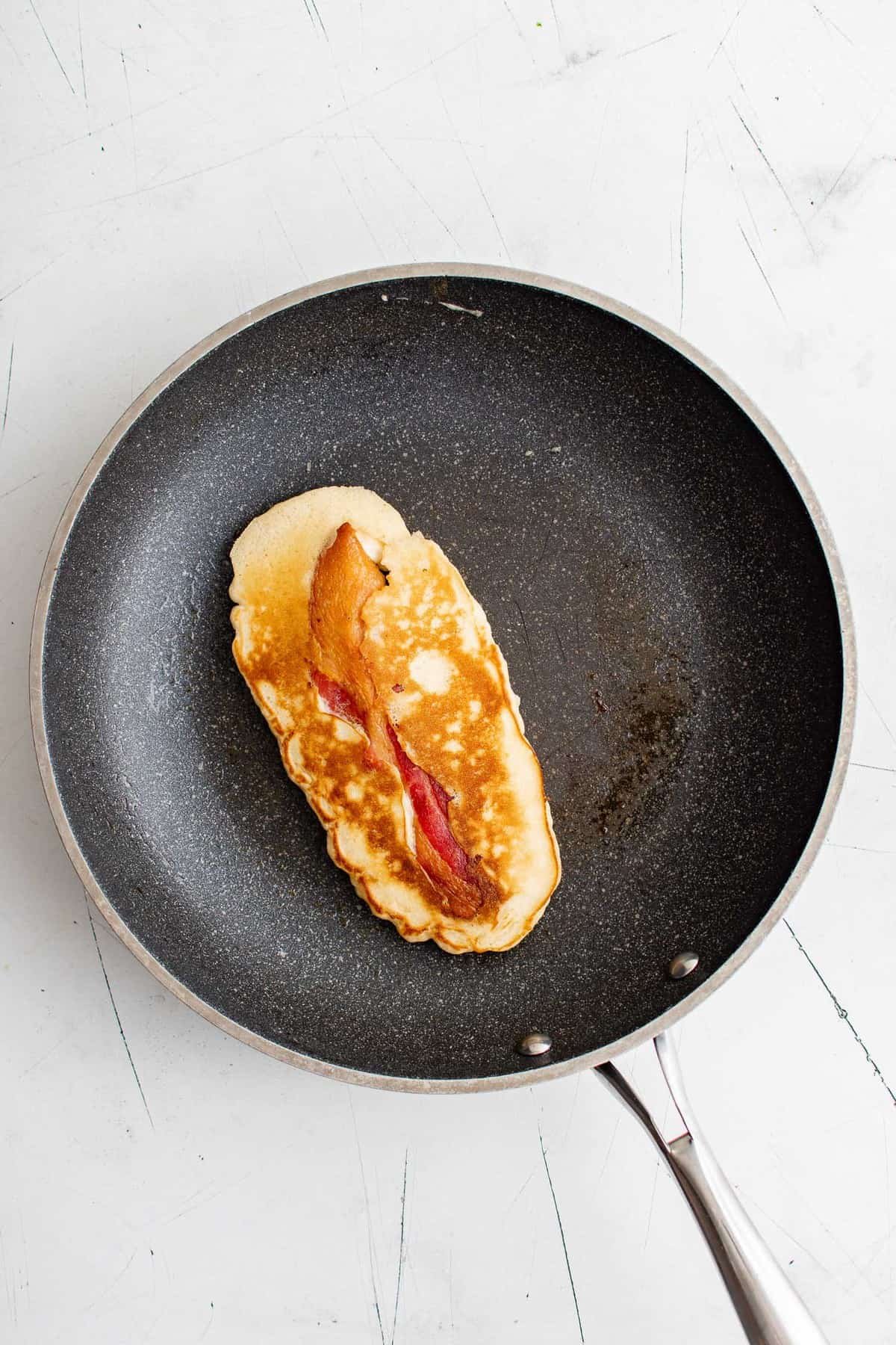 Panqueca com bacon cozida em uma pequena frigideira preta.