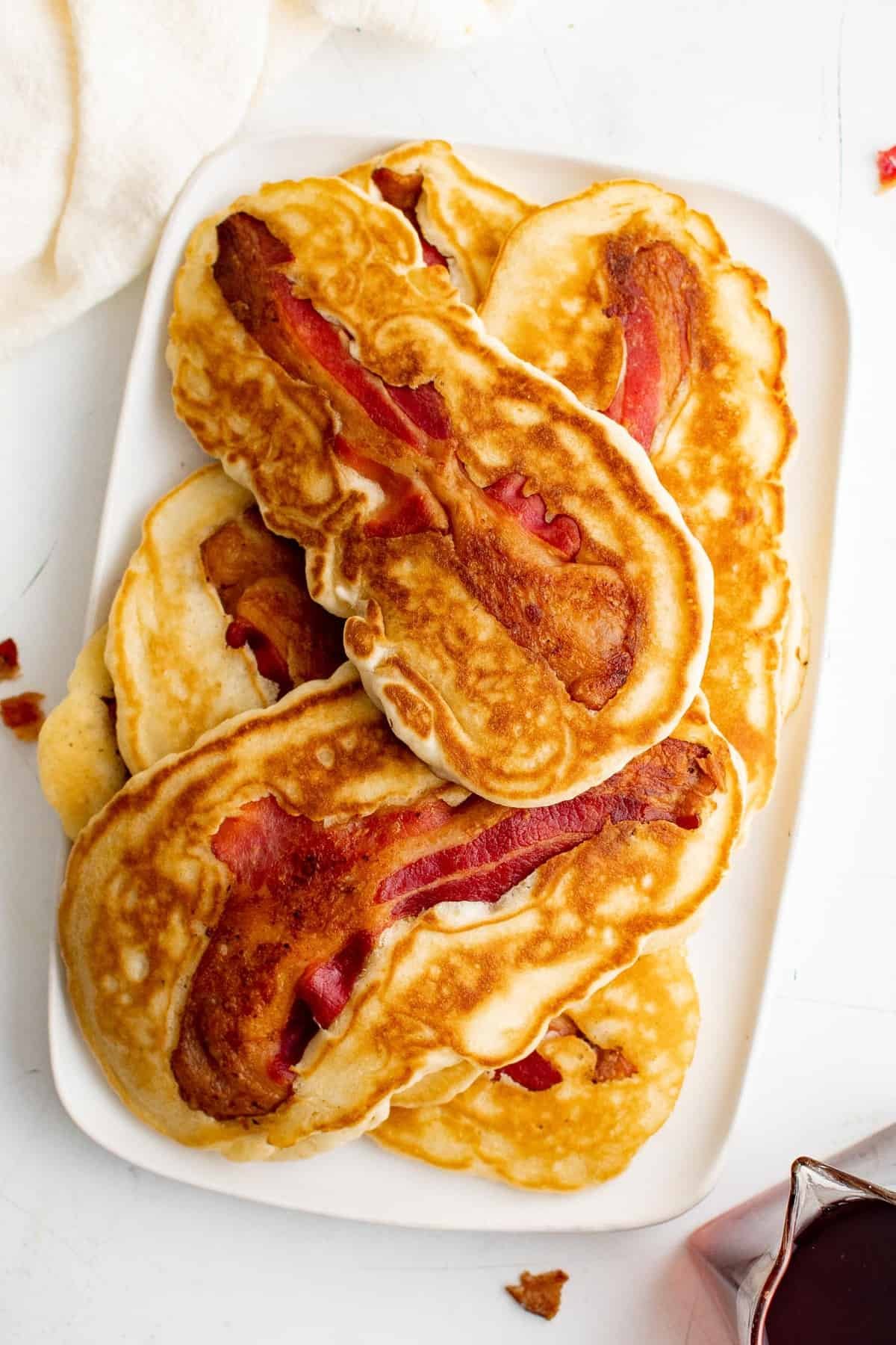 Pilha de panquecas com bacon em um prato retangular branco.