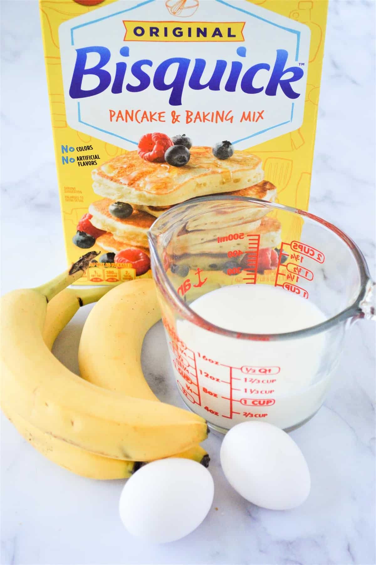 Três bananas, dois ovos, leite em copo medidor e uma caixa de Bisquick.