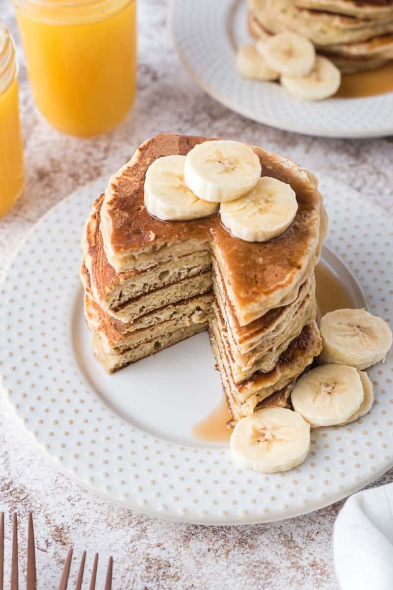 Pilha de panquecas com fatias de banana, com um pedaço cortado das panquecas.