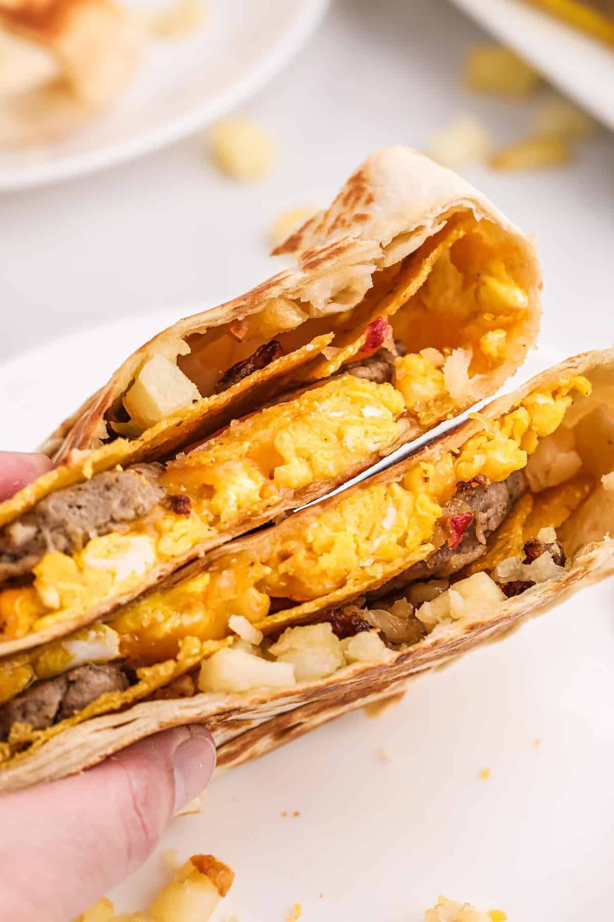 Mão segurando duas metades de um crunchwrap estilo café da manhã.