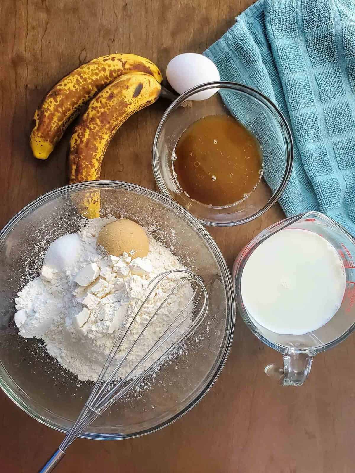 Visão aérea dos ingredientes: farinha, ovo, açúcar mascavo, banana, leite.
