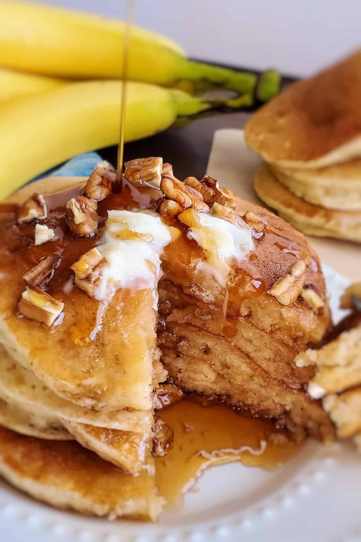 Xarope sendo derramado sobre uma pilha de panquecas cobertas com nozes e manteiga.