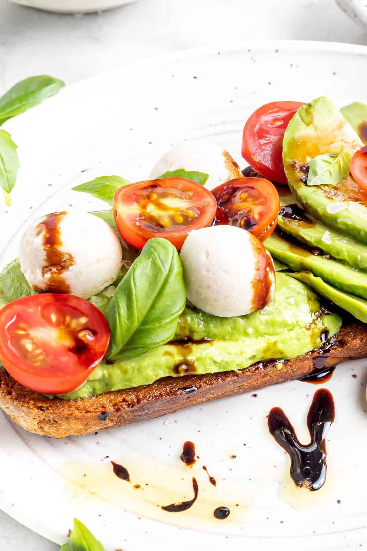 Visão detalhada do toast de abacate coberto com salada caprese.