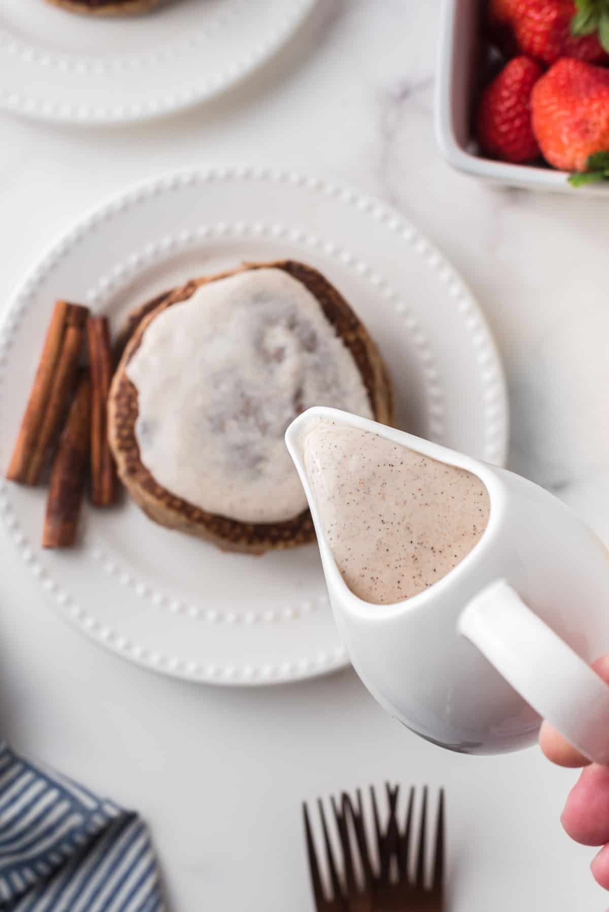 Cobertura de creme de queijo e canela sendo derramada sobre panquecas.