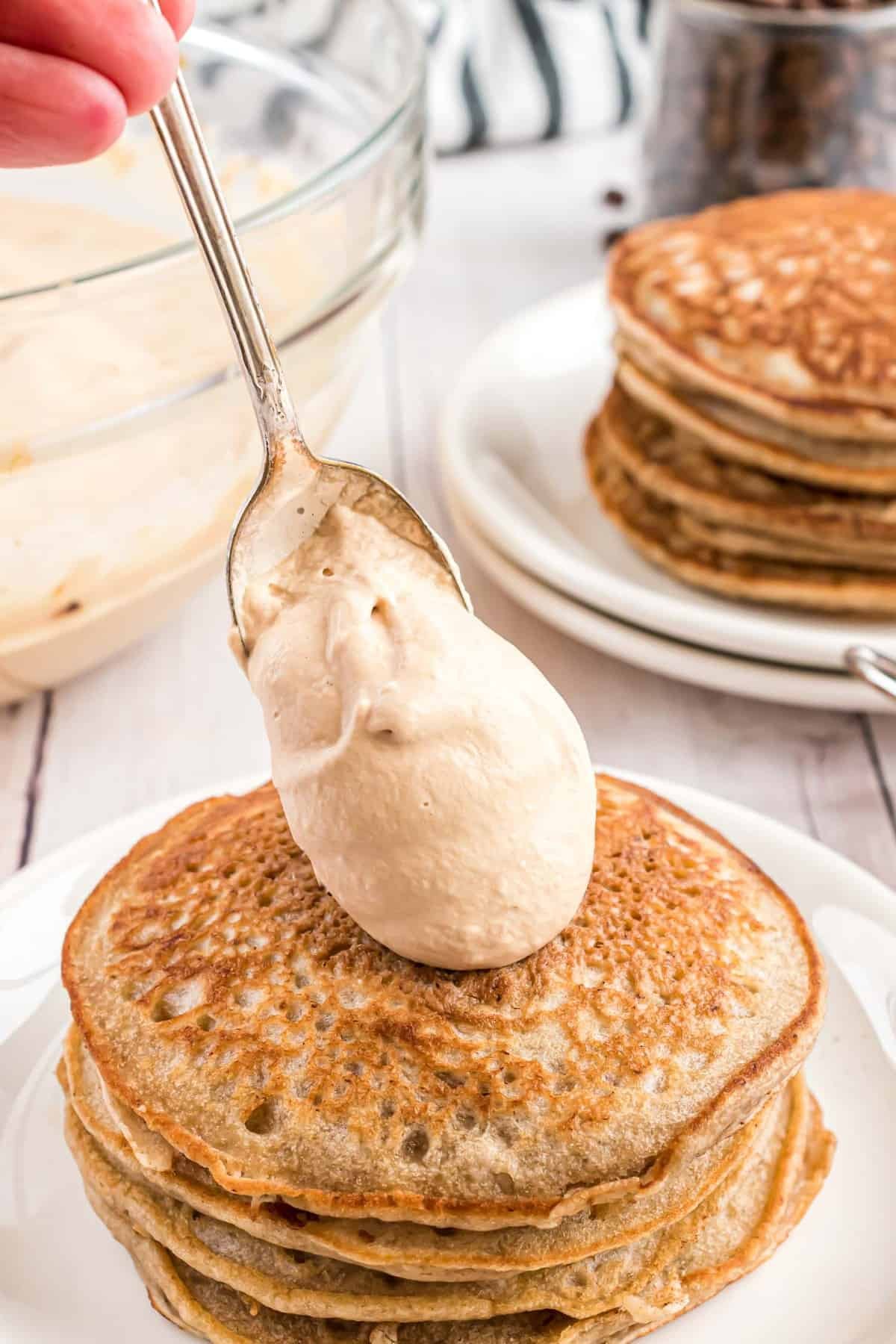 Chantilly sendo colocado em um monte de panquecas.