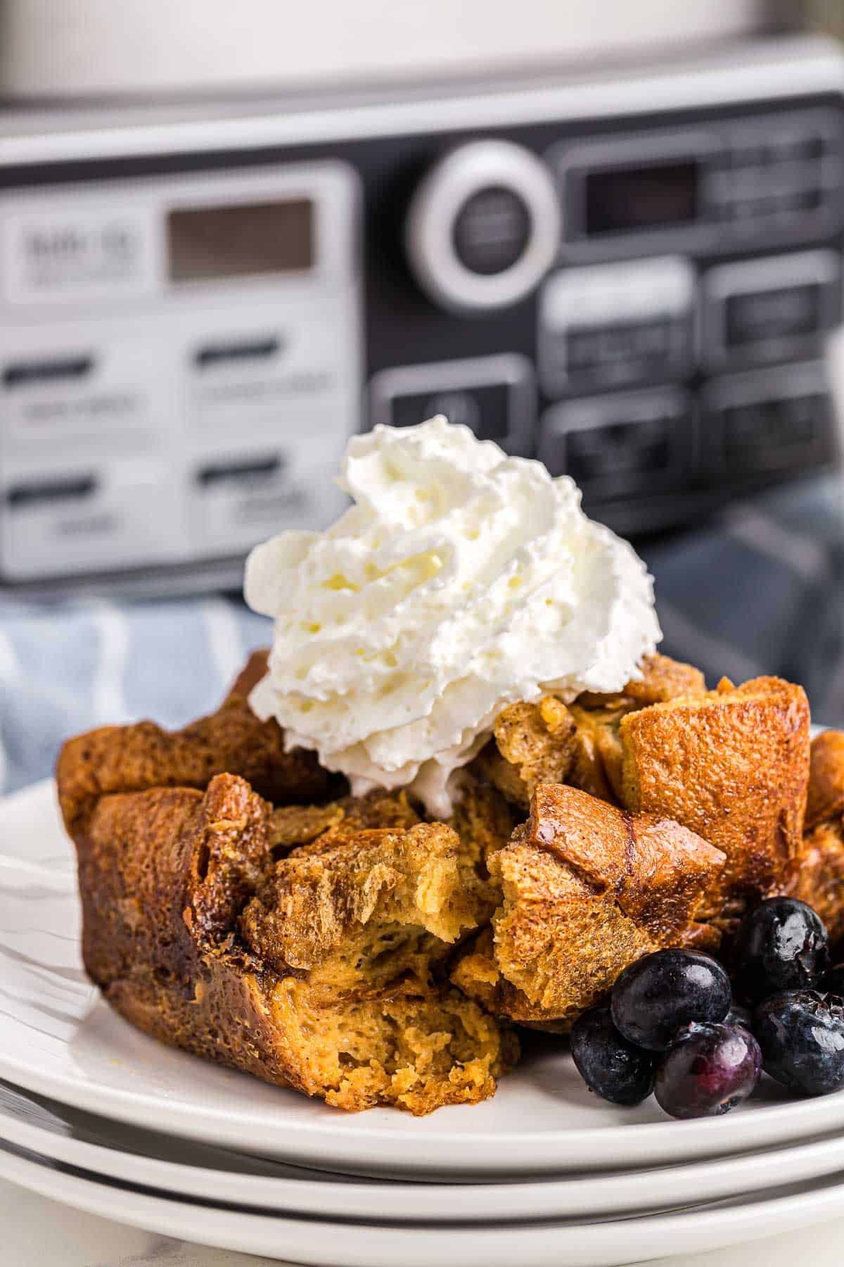 Fatia de casserole de torrada francesa coberta com chantilly, na frente da panela de cozimento lento.