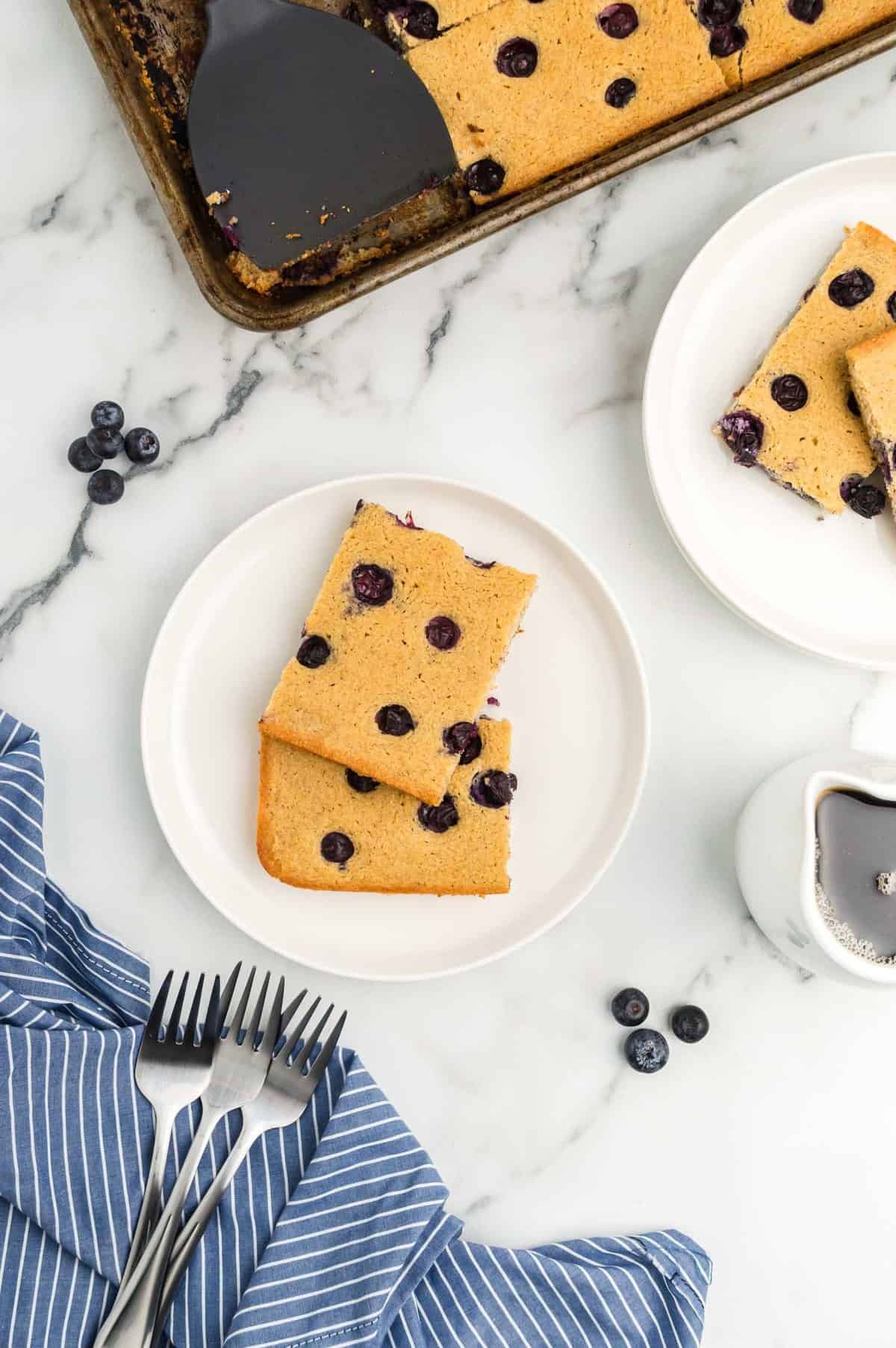 Vista superior de duas panquecas de mirtilos quadradas em um prato branco.