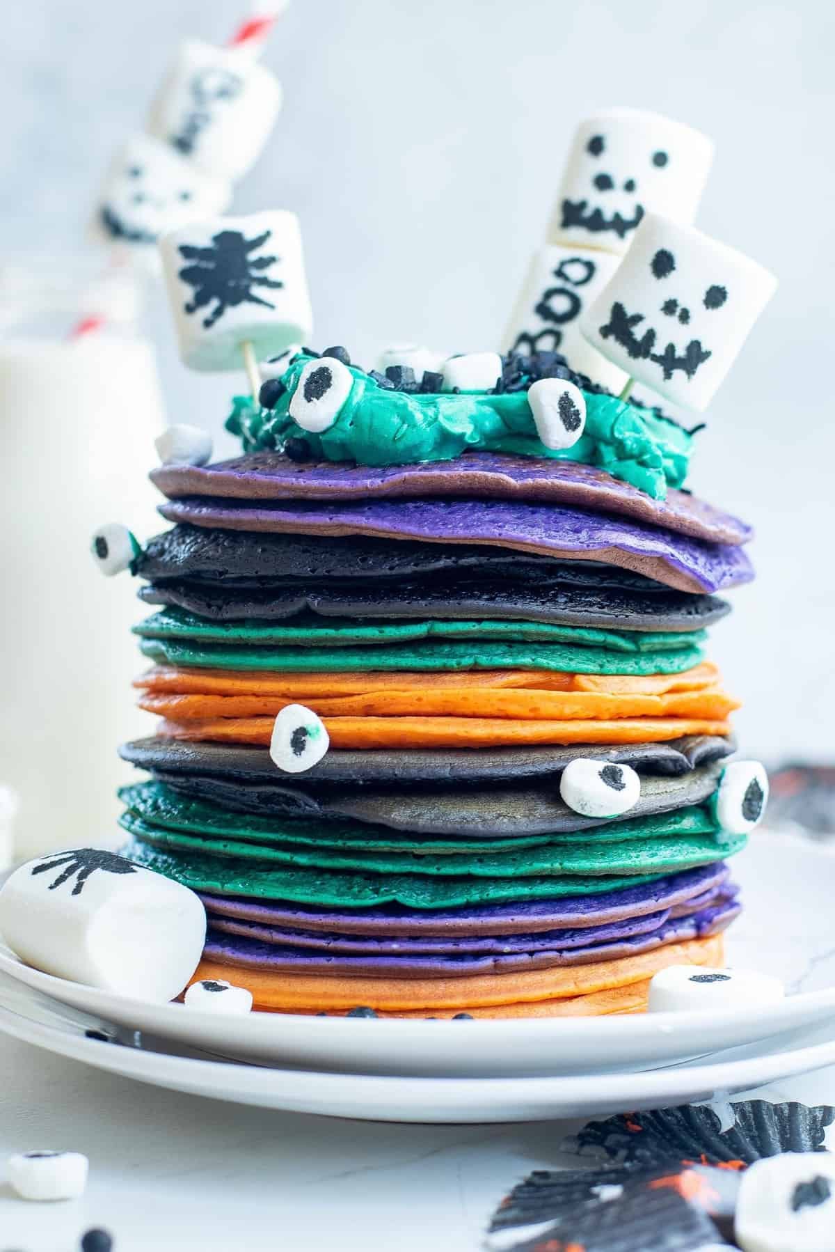 Pilha de panquecas de Halloween multicoloridas com marshmallows decorados.