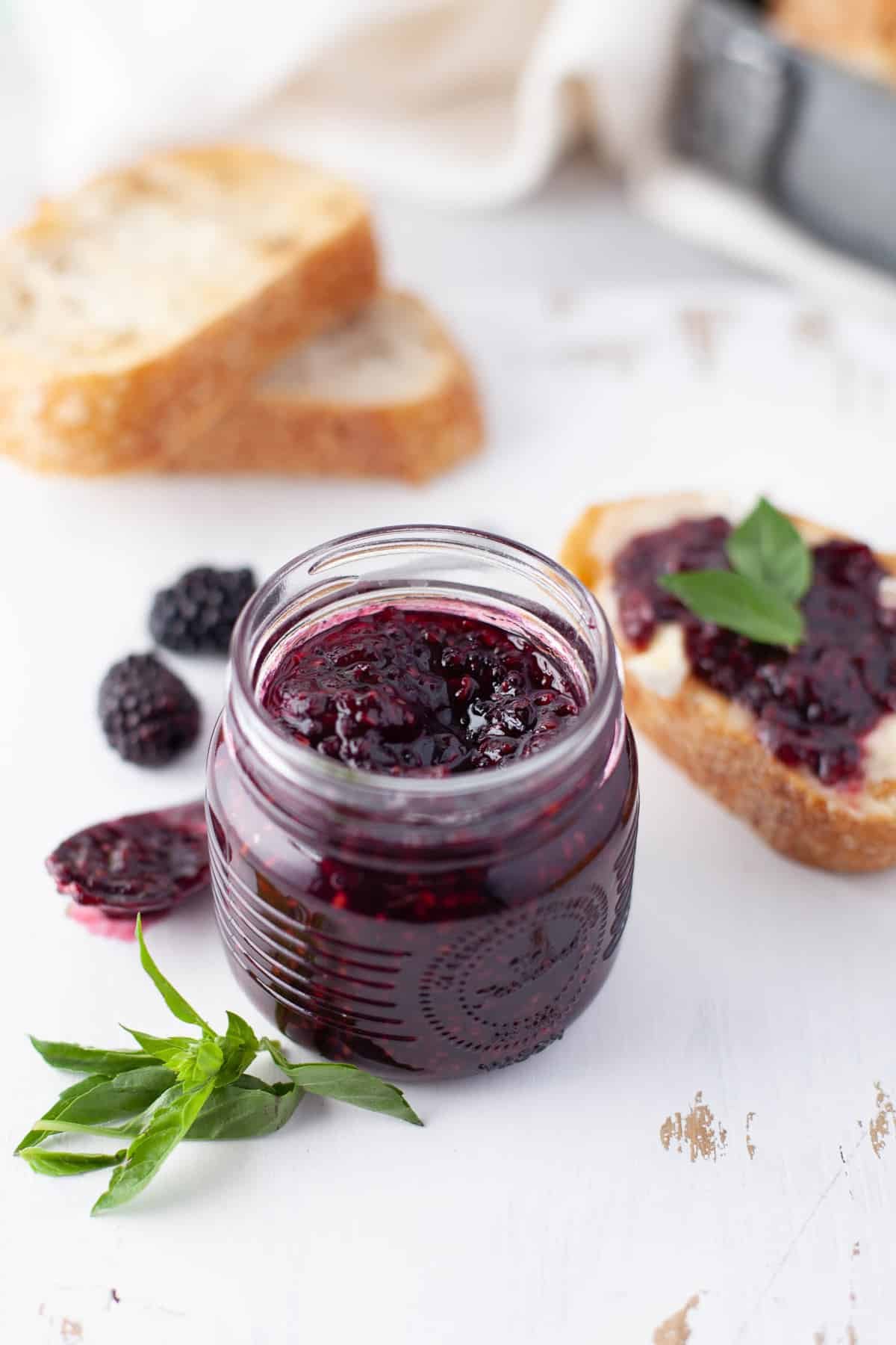 Geleia de frutas vermelhas saudável em um pequeno pote, torrada com geleia ao fundo.