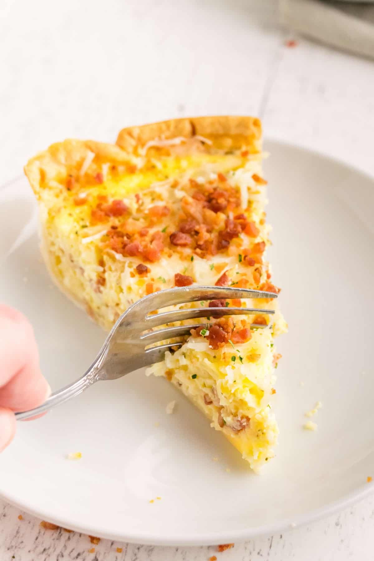 Fatia de quiche em um prato branco, um garfo cortando.