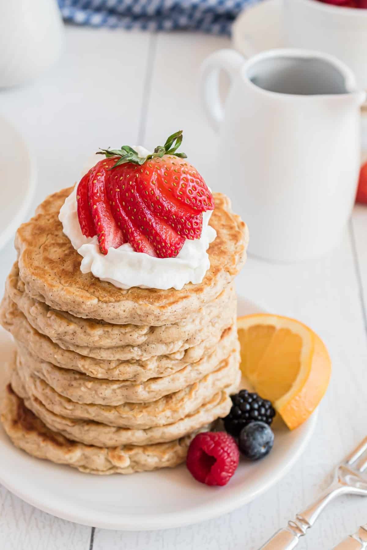 Panquecas de aveia empilhadas em altura, cobertas com chantilly e um morango.