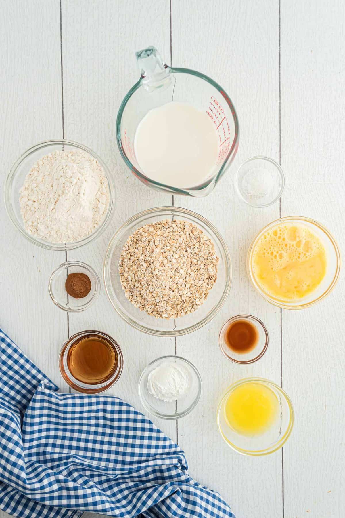 Visão aérea de tigelas de ingredientes: aveia, farinha, manteiga, baunilha, canela e mais.