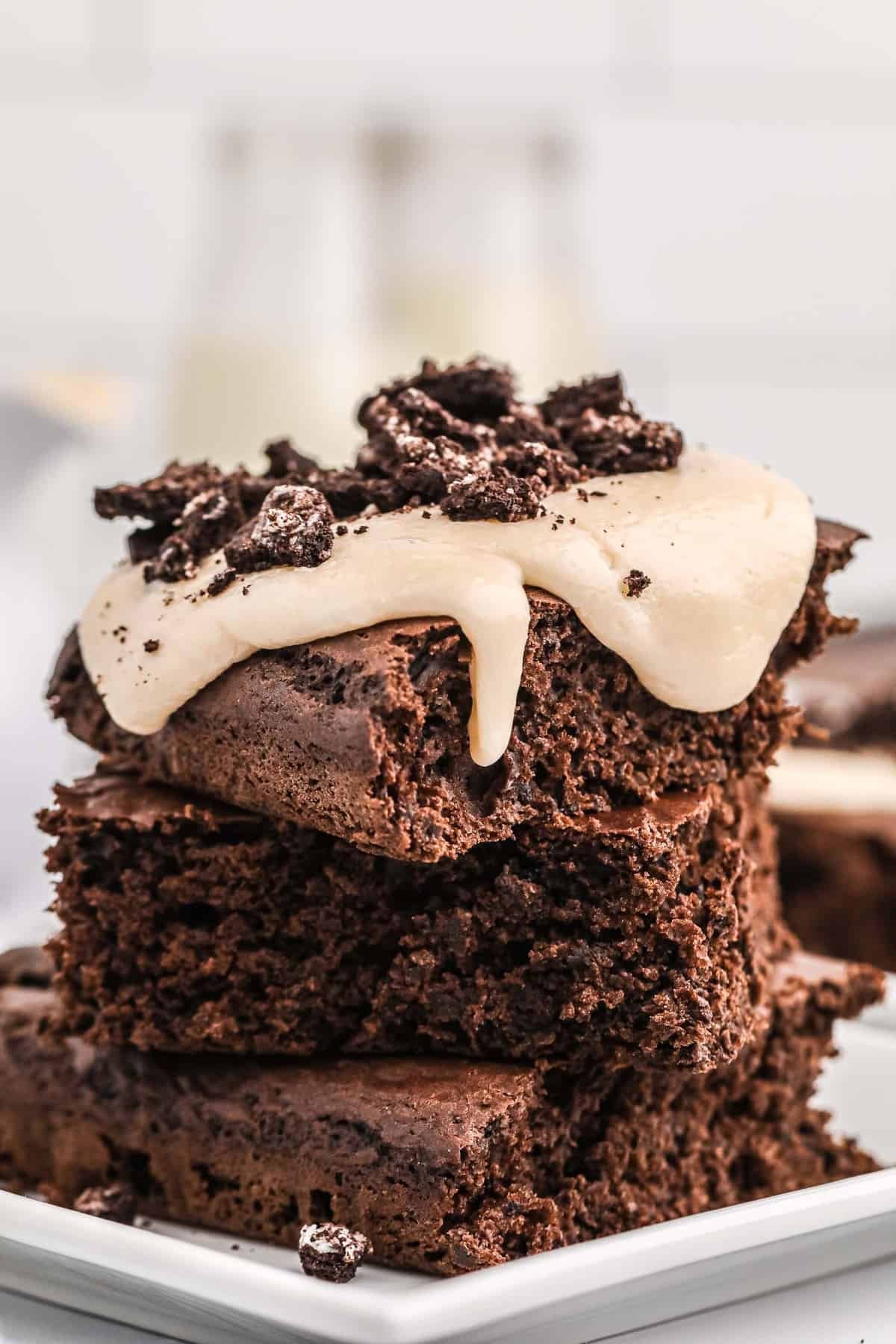 Pilha de panquecas de chocolate cortadas em quadrados, cobertas com um cobertura cremosa e bolachas Oreo esmagadas.