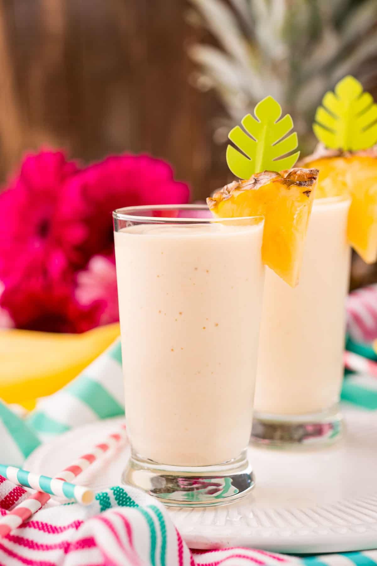 Dois copos altos com batido de abacaxi, cobertos com abacaxi fresco.