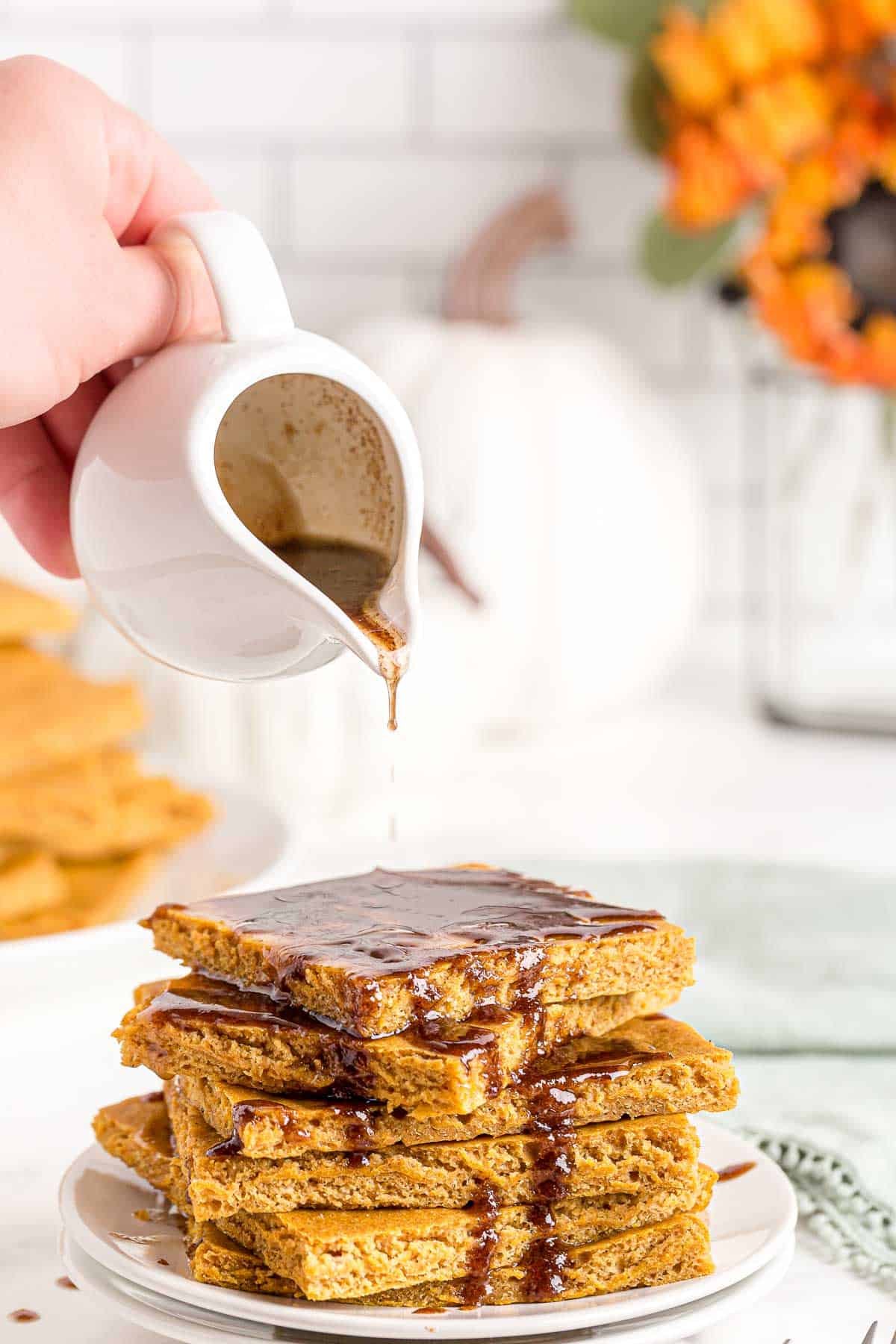 Pilha de fatias de panqueca de abóbora na assadeira, sendo cobertas com fio de manteiga de canela.