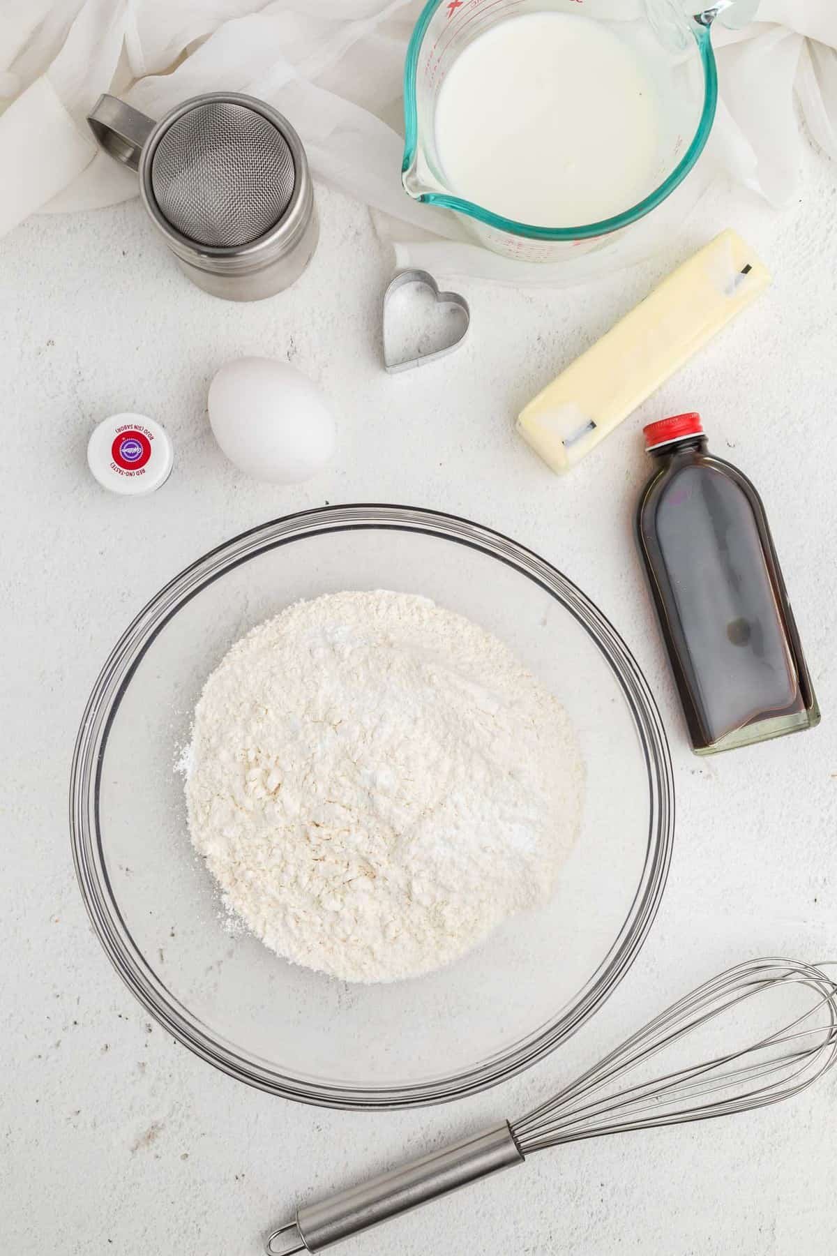 Ingredientes secos em uma tigela com outros ingredientes ao redor, incluindo baunilha e manteiga.