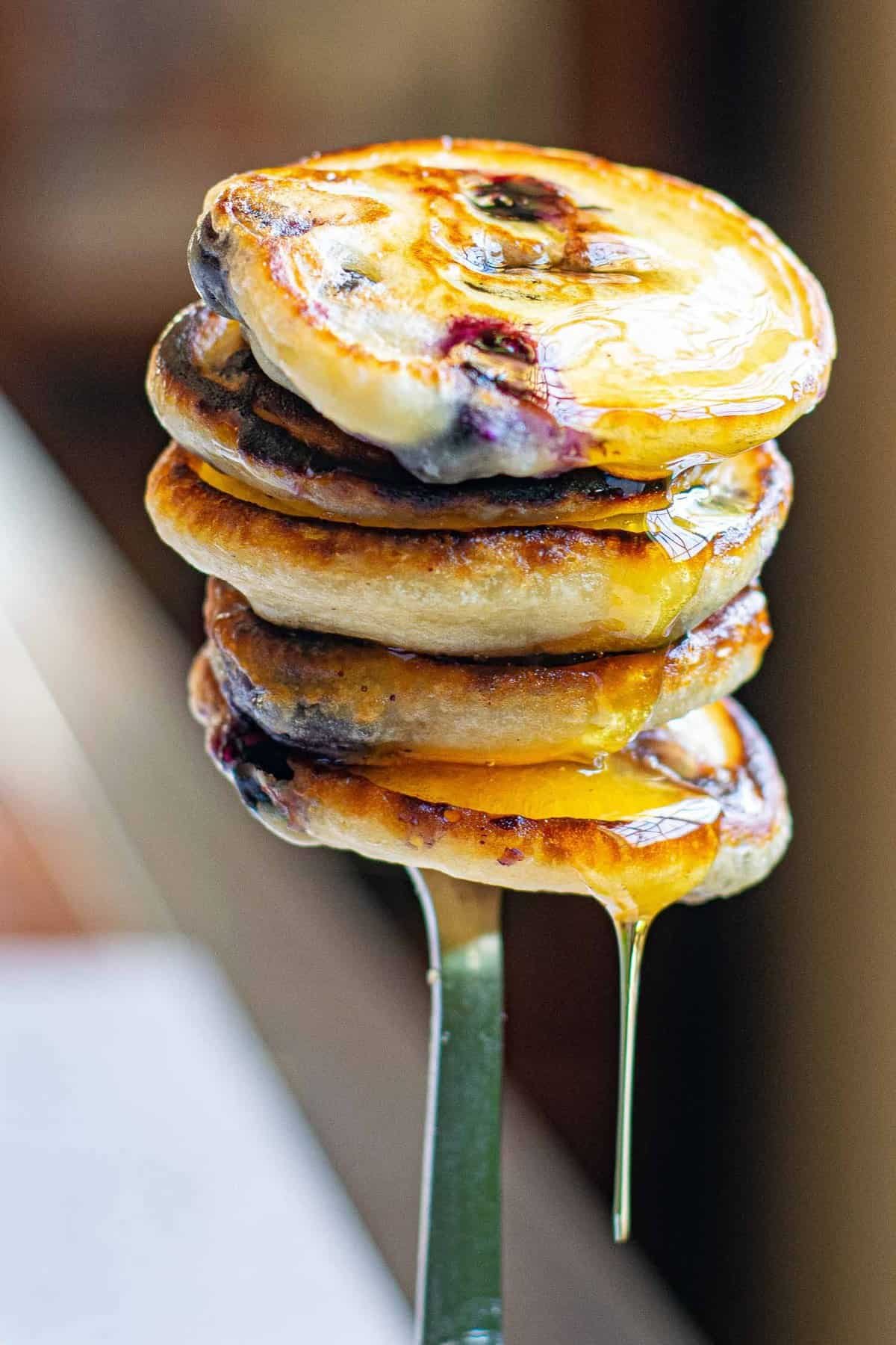 Pilha de pequenas panquecas veganas de mirtilo em um garfo, pingando com xarope.