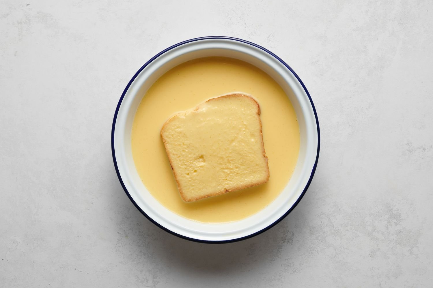 A piece of bread soaking in the whisked egg and milk mixture
