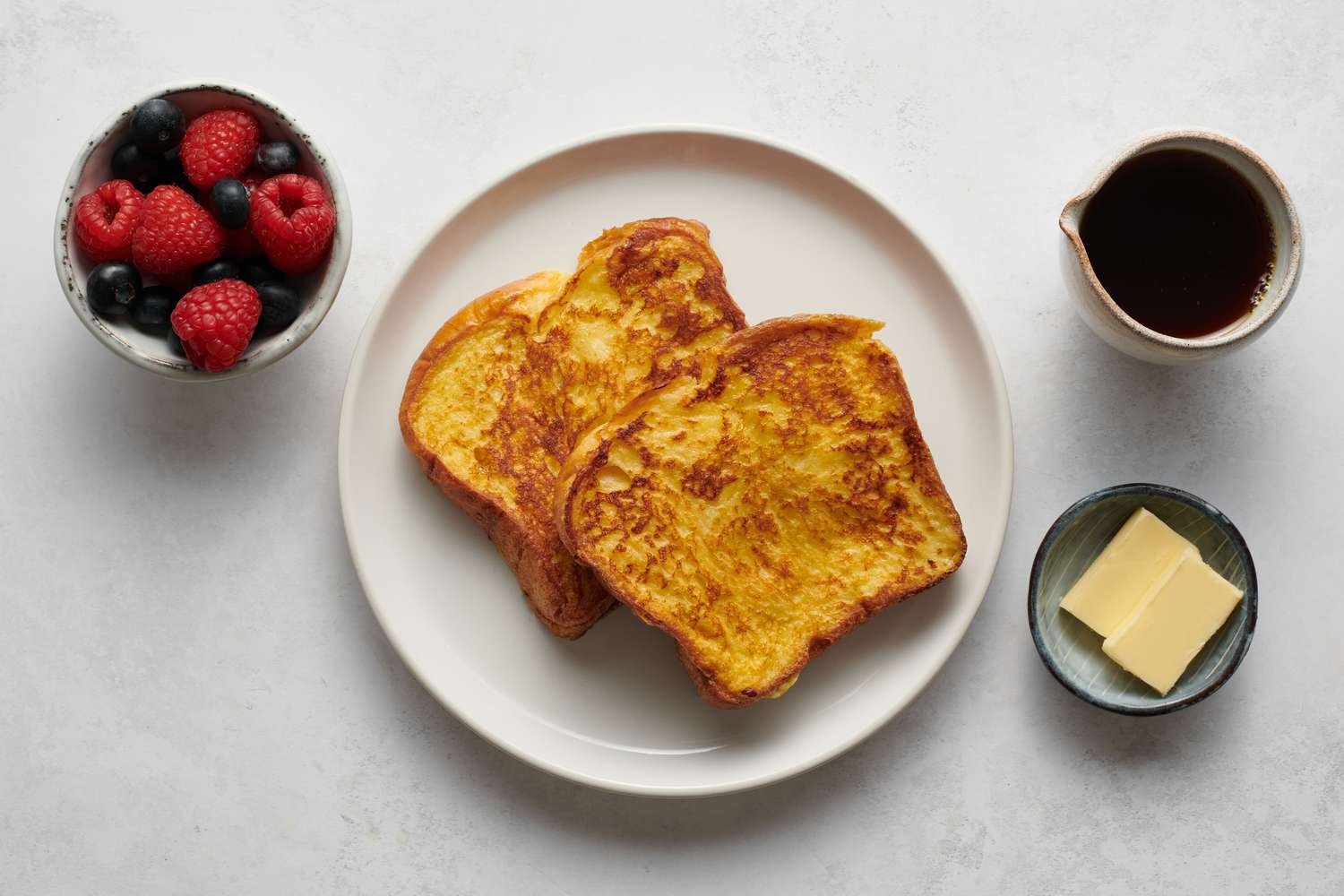 A plate of French toast served with butter, syrup, and berries