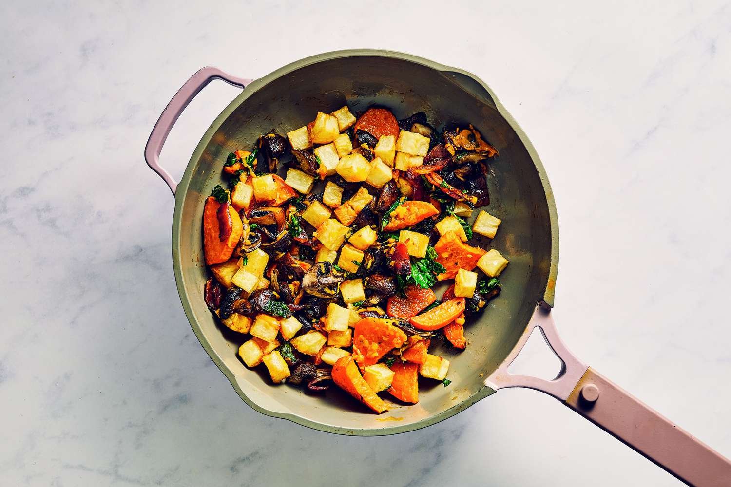 A skilled of breakfast potatoes, roasted sweet potatoes and mushrooms, chopped kale, and shredded Jack cheese