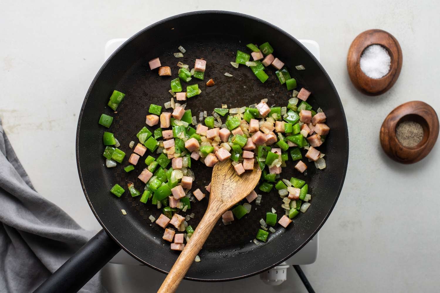Ham and bell pepper being stirred in with a wooden spoon in a frying pan