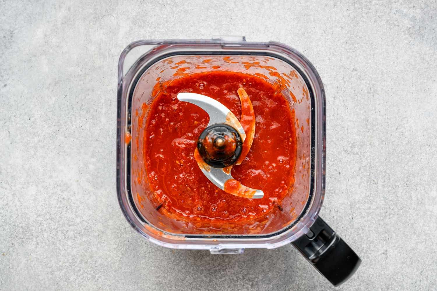 A blender with a sauce made from blended chiles de arbol, guajillo chiles, Roma tomatoes, and garlic