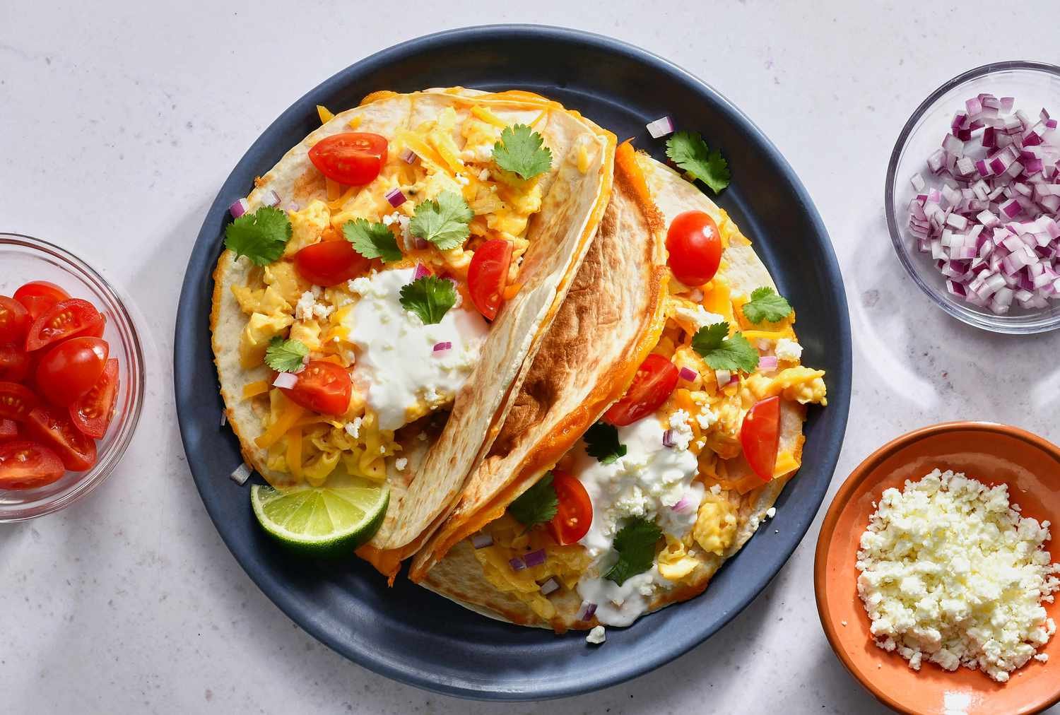 Breakfast quesadilla tacos topped with cilantro, sour cream, and tomatoes