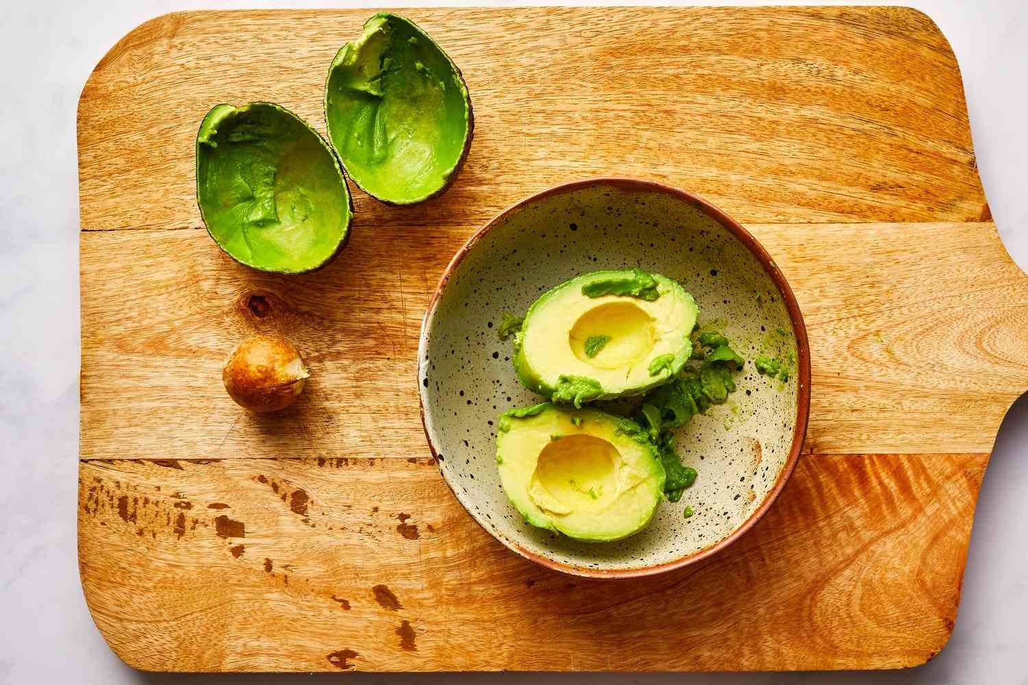 avocado peeled and seeded on cutting board resting in a bowl