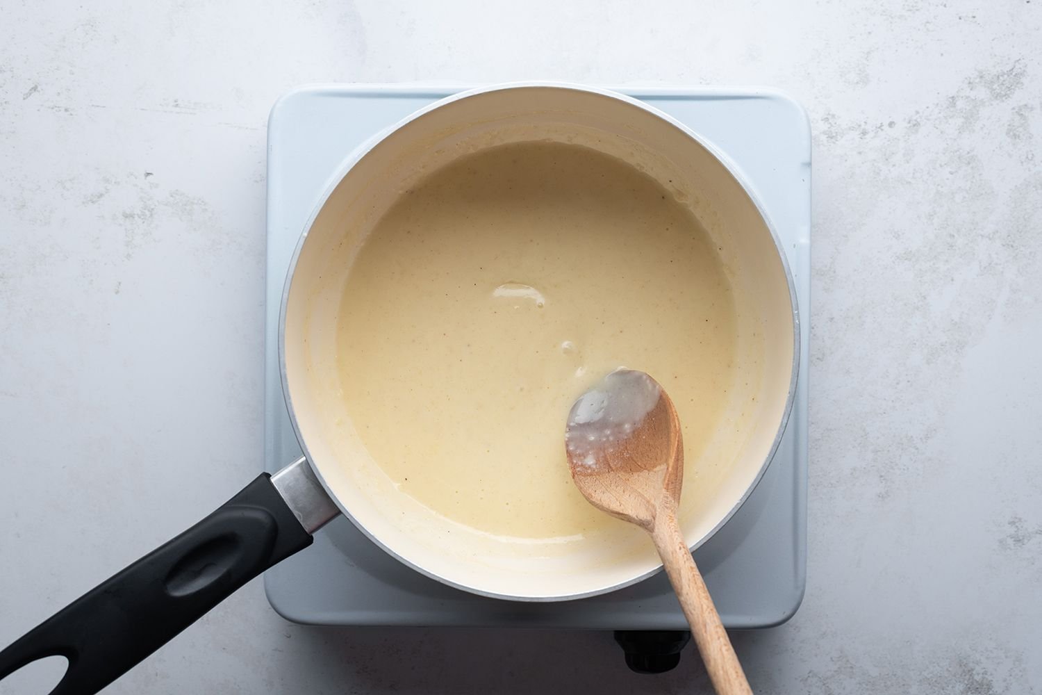 Béchamel sauce in a saucepan with a wooden spoon, on a burner