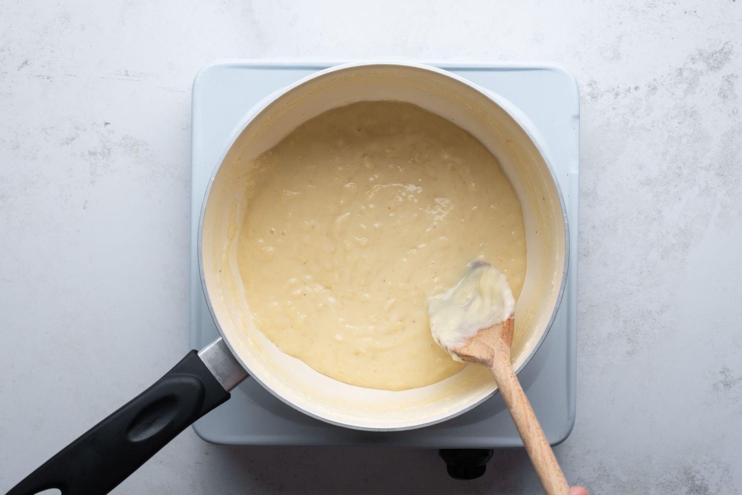 Cheese sauce in a saucepan with a wooden spoon on a burner