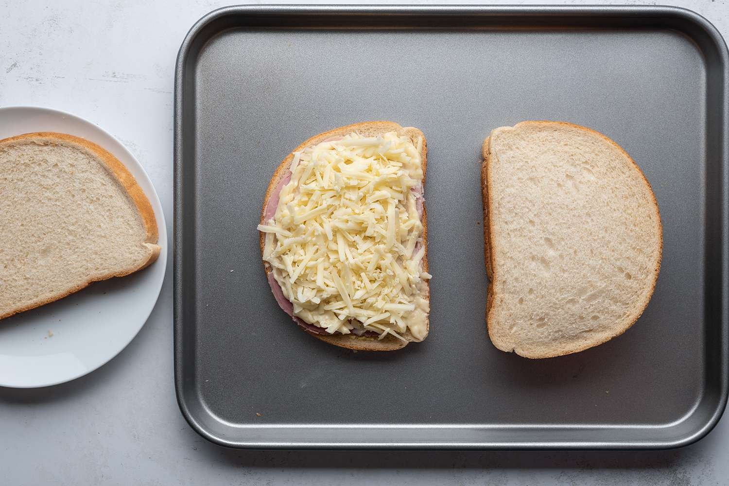 Cheese, bread and ham sandwiches on a sheet pan, and bread on a plate