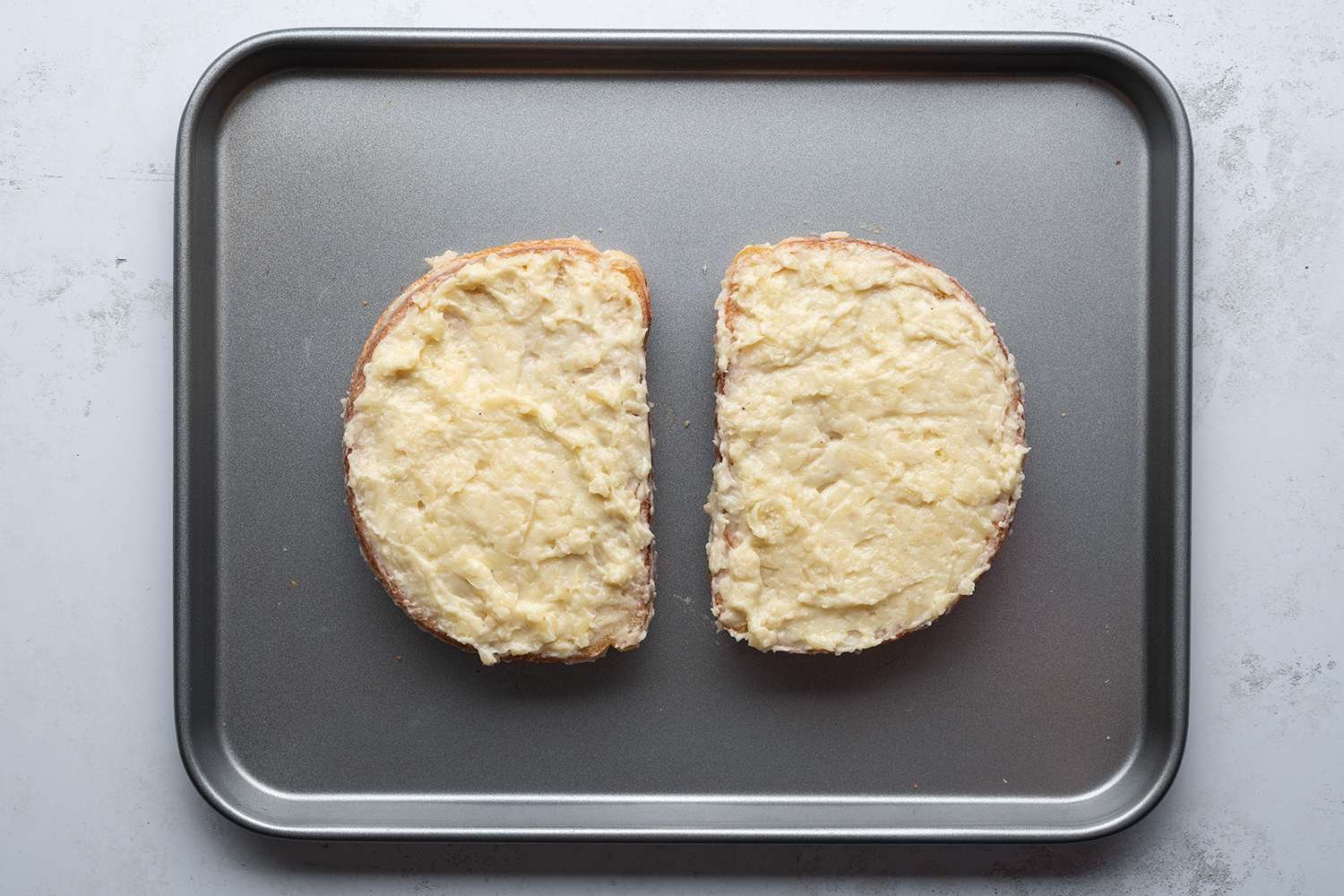 Sandwiches coated with a cheese mixture on a sheet pan