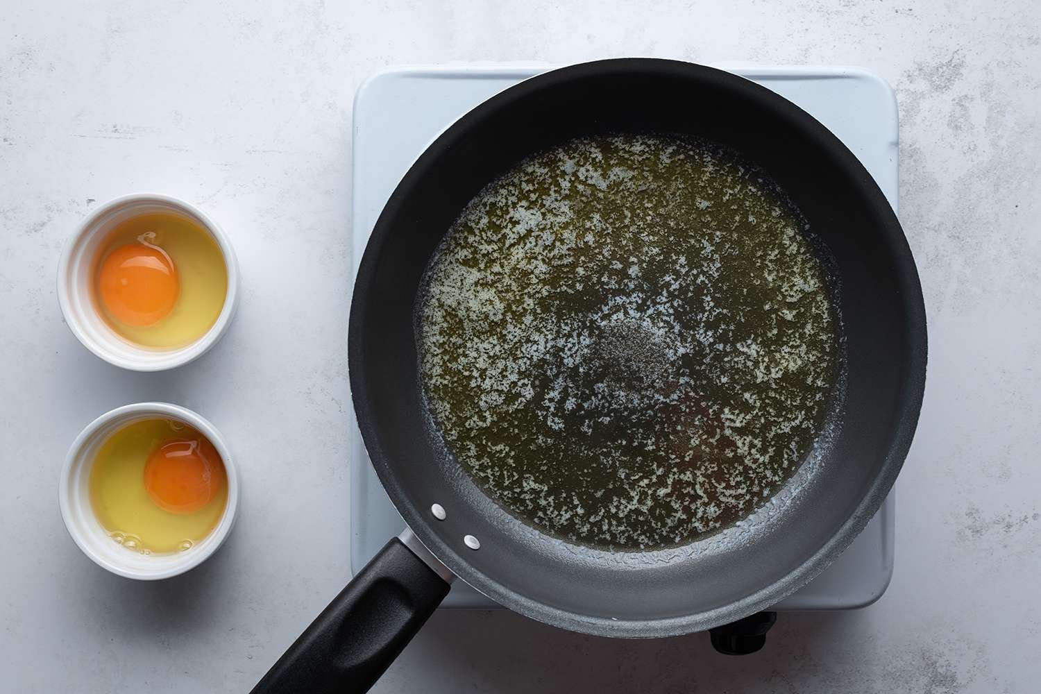 Eggs in ramekins and a pan with butter on a burner