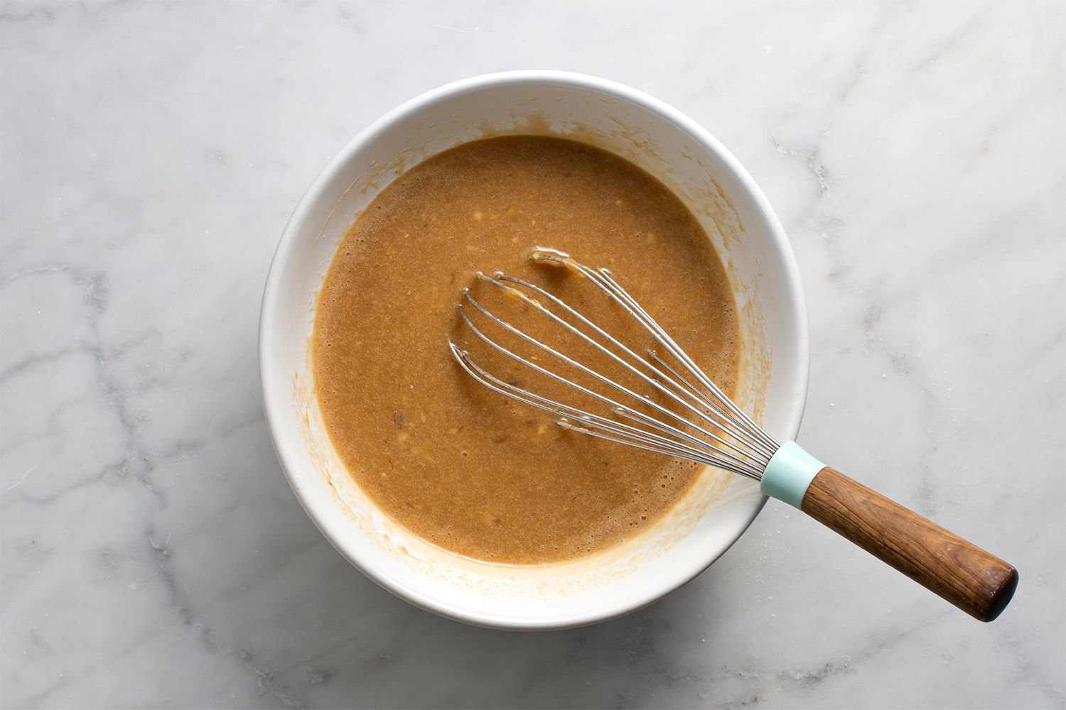 Bananas, milk, melted coconut oil, egg, brown sugar, granulated sugar, and vanilla in a bowl with a whisk