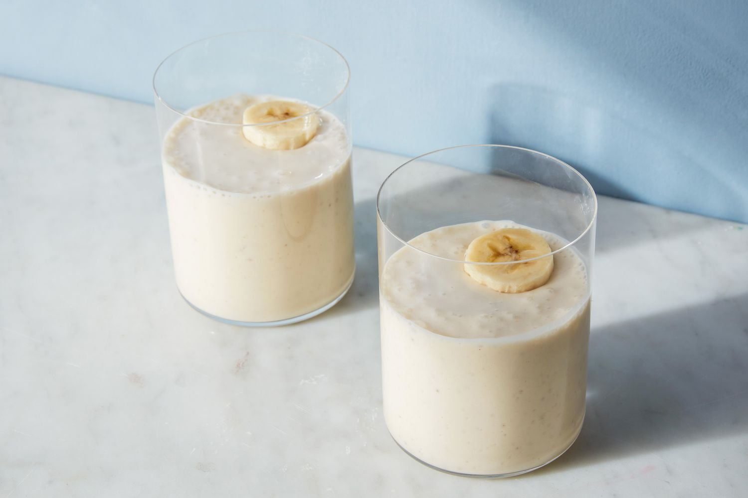Two glasses of banana smoothies, garnished with sliced bananas