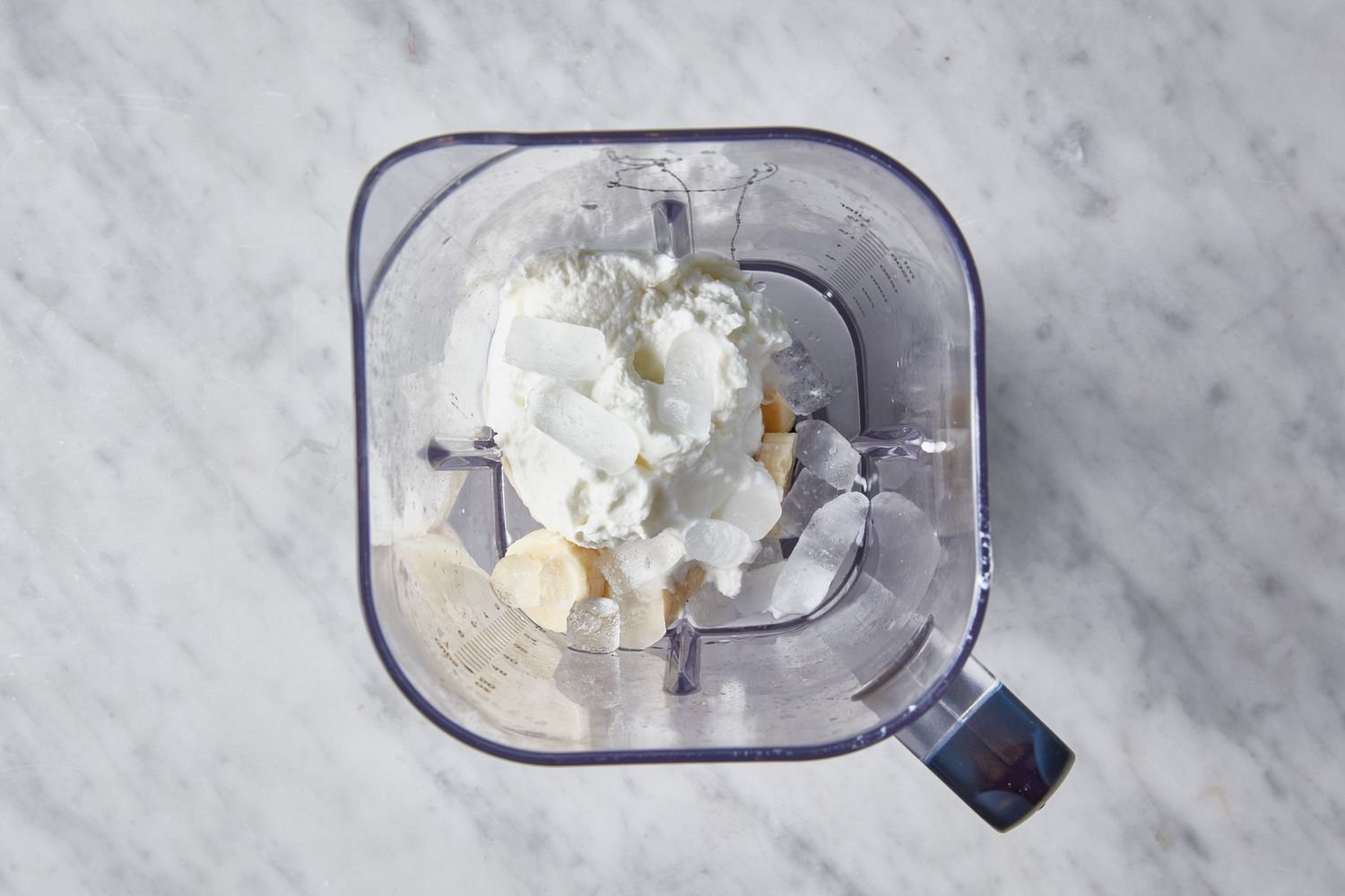 A pitcher of a blender with honey, vanilla, ice, sliced bananas, and yogurt