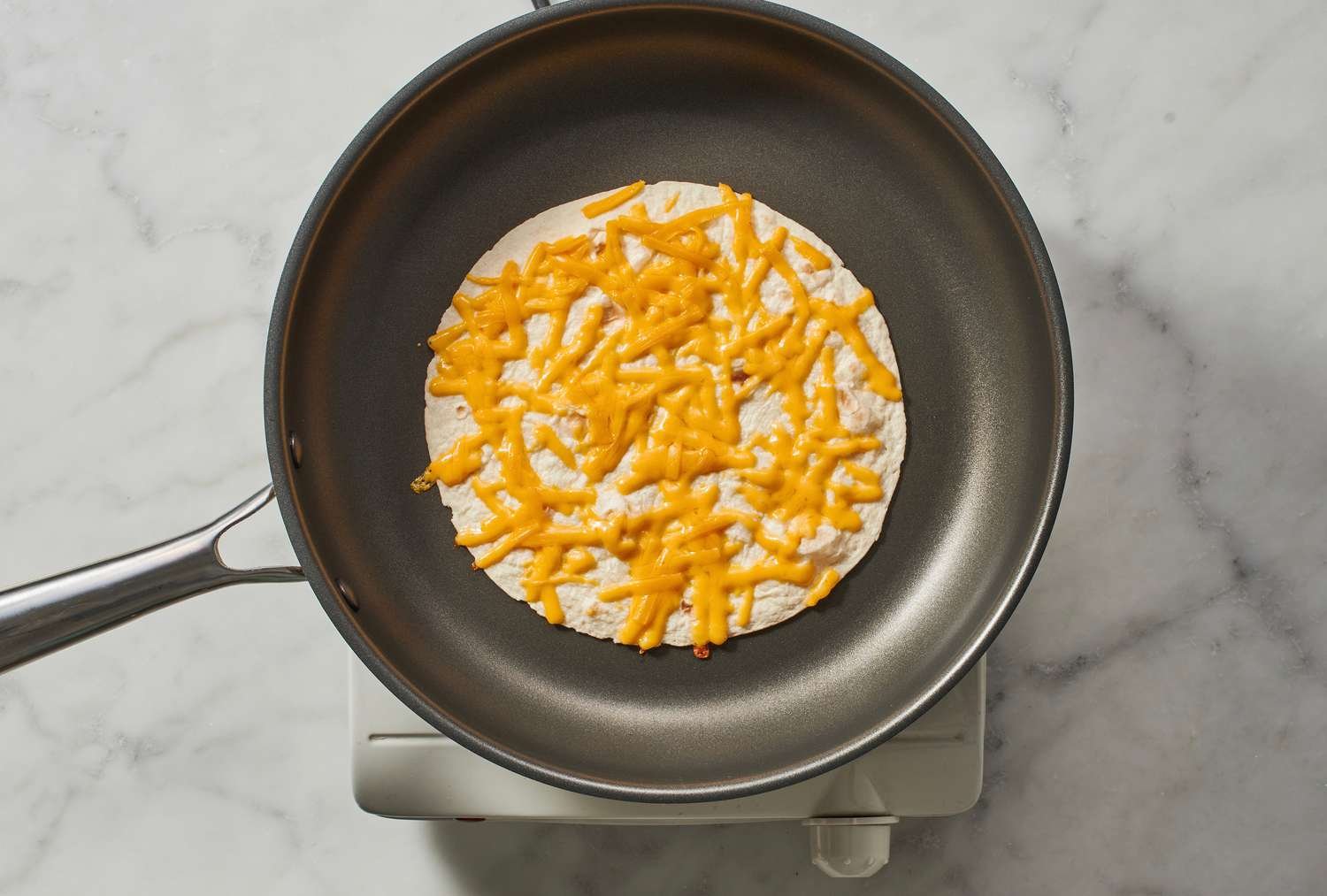 A tortilla topped with shredded cheese in a skillet