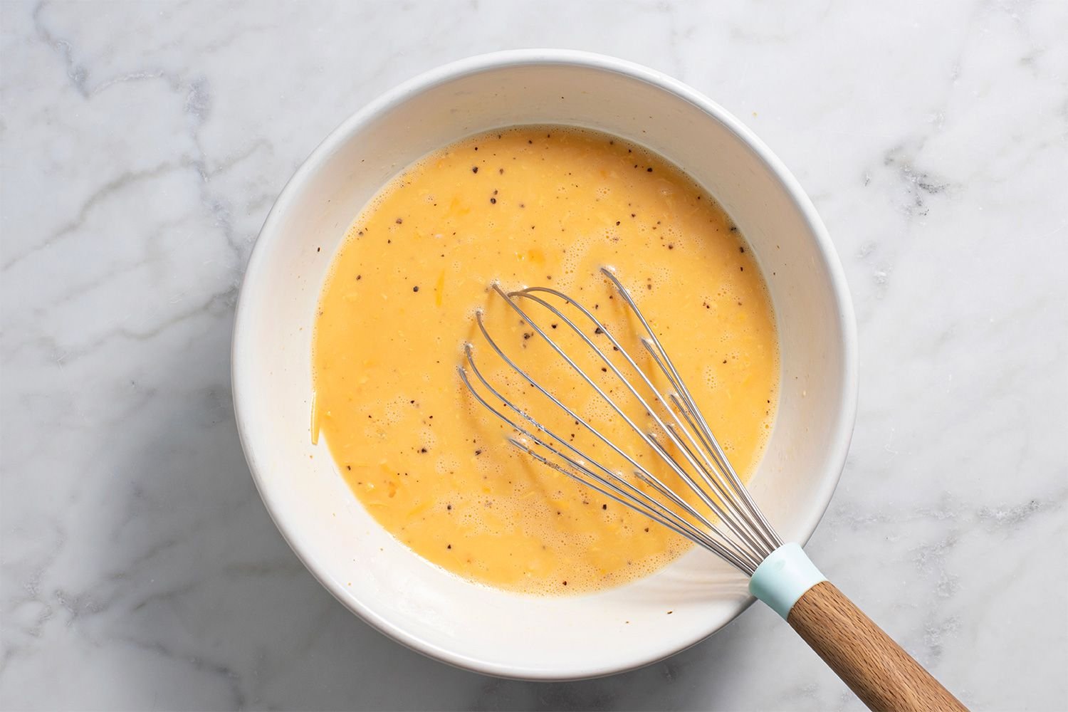 Eggs whisked together in a bowl with shredded cheese, half-and-half, salt, pepper, and nutmeg