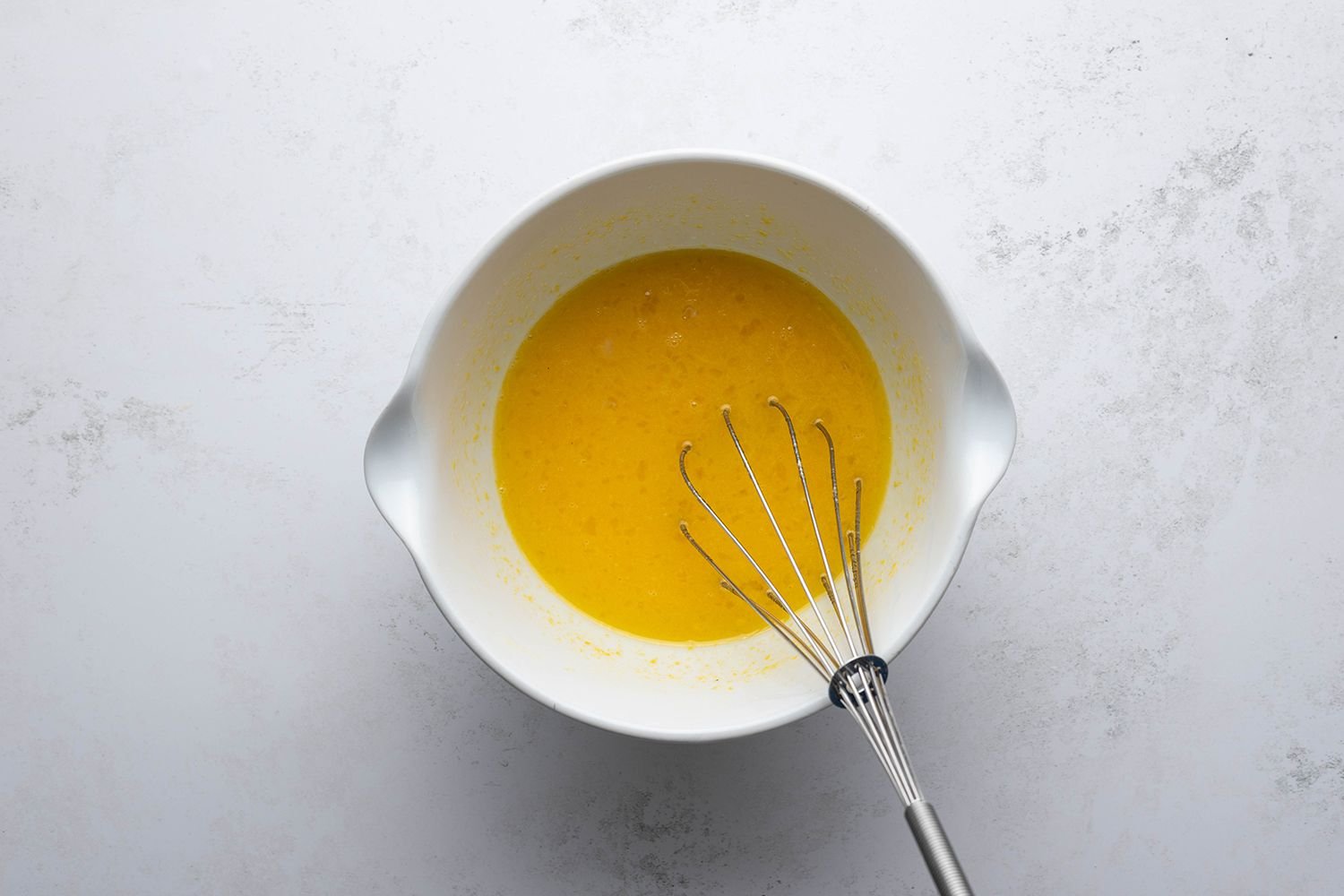 Bowl with eggs, sugar, and lemon mixture being whisked